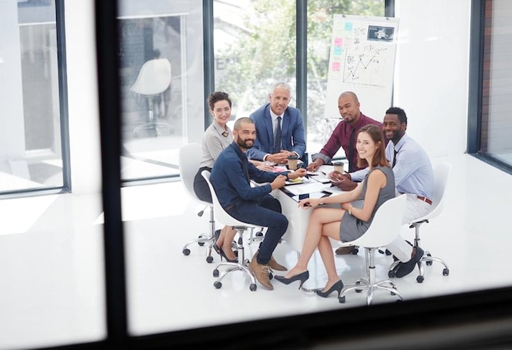 Five colleagues seated around a meeting table, seen from above through a glass wall