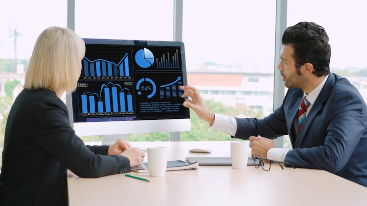 Two colleagues reviewing charts on a desktop monitor
